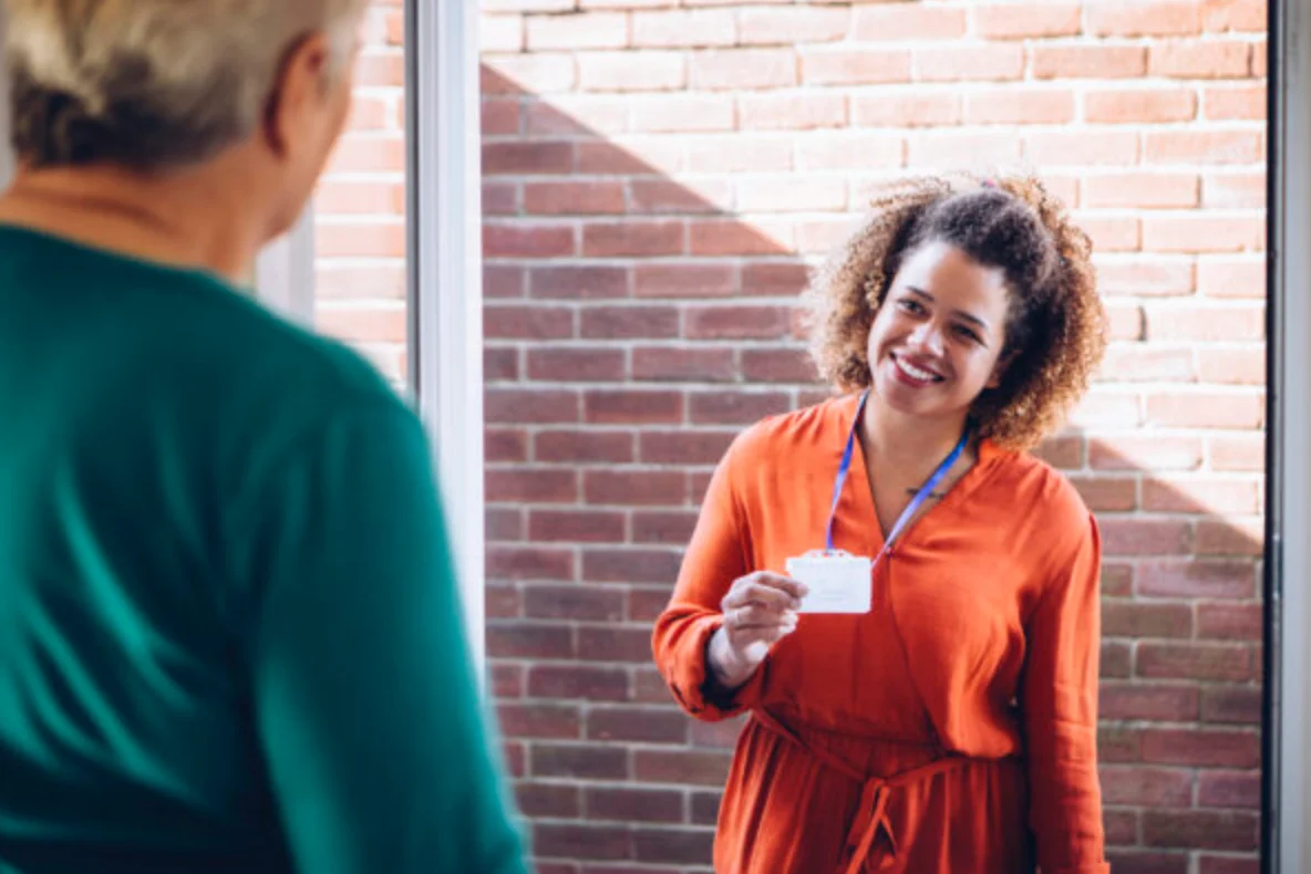 Healthcare worker showing her badge at the front door of a senior womans home.